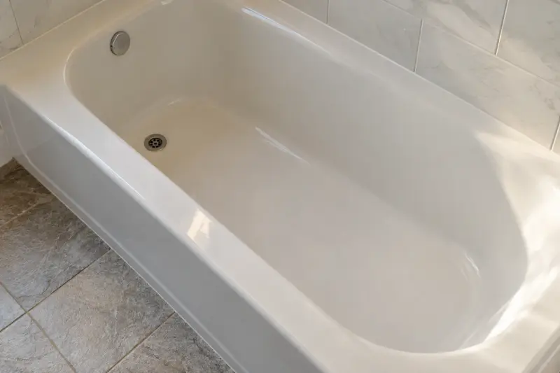 Illustrative dry bathtub surface beside textured bathroom floor tiles.
