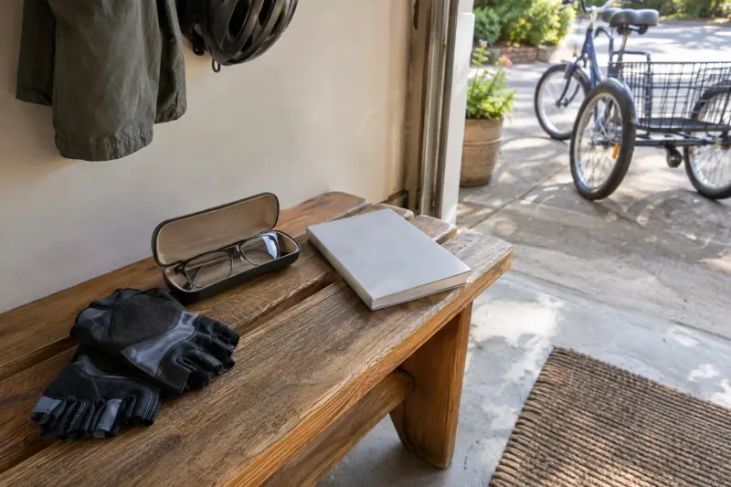 Illustrative preparation items on an entry bench: cycling gloves, glasses and a closed plain manual, with a tricycle beyond the doorway.