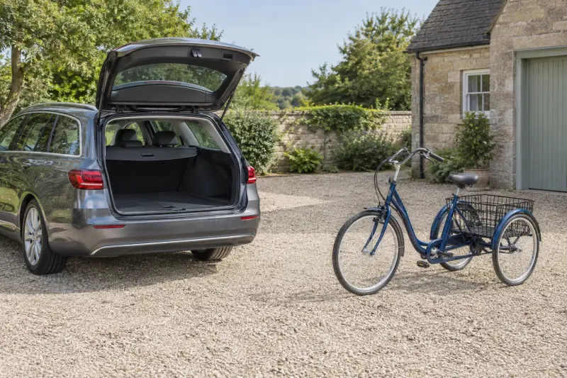 Illustrative transport planning with an empty open car boot and a generic tricycle standing separately on a driveway.