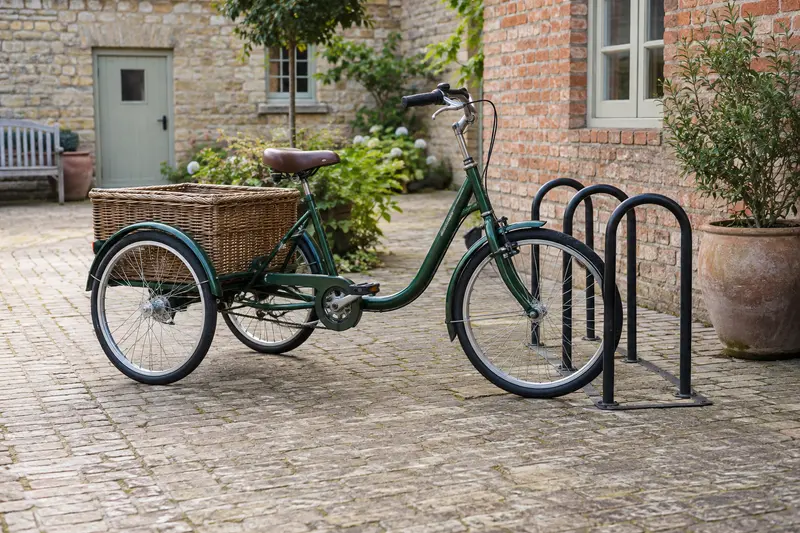 Illustrative parked adult tricycle beside a cycle stand in a brick courtyard.